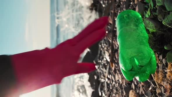 A volunteer in rubber gloves picks up a plastic bottle.Vertical orientation.