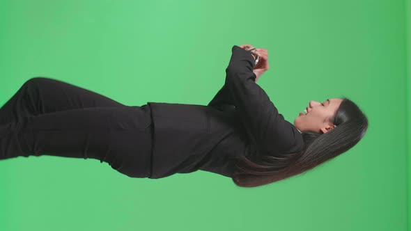 Side View Of A Smiling Asian Business Woman Looking At A Watch While Walking On Green Screen