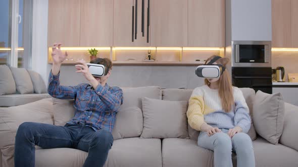 Young couple at home on the couch in a VR helmet.People wearing glasses, a reality helmet.