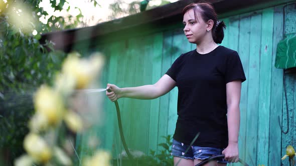 Young Woman Watering Vegetable Garden From Hose. Close Up of Female Watering. Concept of Summer and