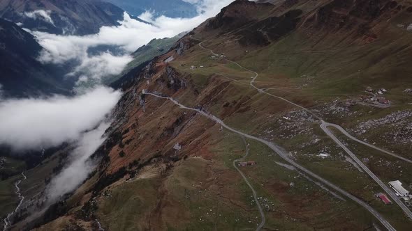 Clouds hang in the valley of rocky mountain landscape criss-crossed by winding roads