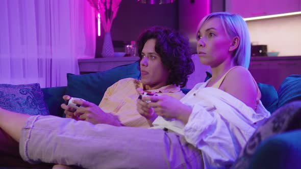 Happy Young Couple Playing a Video Game Sitting at Home on a Sofa During Self Isolation on