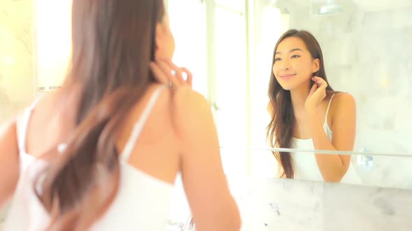 Beautiful asian woman looking at a mirror and touching face