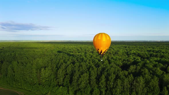 A yellow nylon balloon flies over the forest. Propane burner shoots out a flame