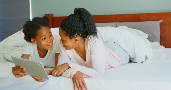 Front view of mid adult black mother and daughter using digital tablet on bed in comfortable home 4k