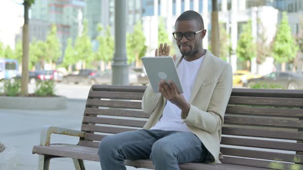 Online Video Chat on Tablet By African Man Sitting Outdoor on Bench