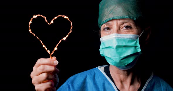 Female Doctor Holds Heart Symbol in Hand with Black Background.