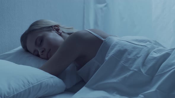 Young woman lying in the bed at night. Beautiful sleeping girl. Twilight in the bedroom.