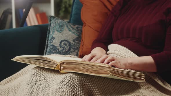 Blind Woman Reading Braille Book Using Fingers Sitting on Sofa in Living Room Poorly Seeing Female