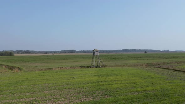 Drone footage flying near a wooden hunting lookout in the middle of crop fields on farmland in rural