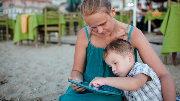 Mother And Son Using Tablet Pc Near Beach Cafe