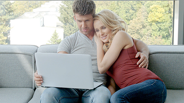 Young Couple Sitting On Couch With Laptop