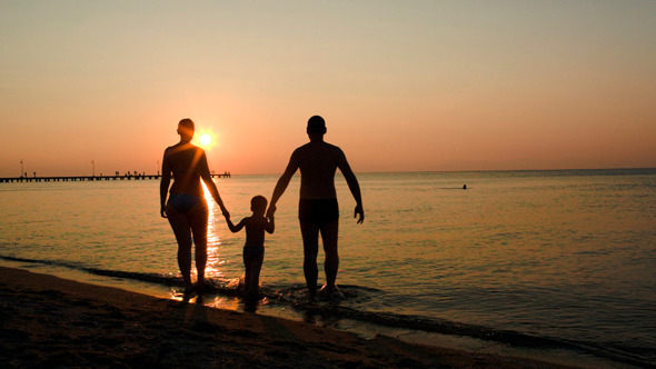 Parents And Child Bathing In The Sea At Sunset
