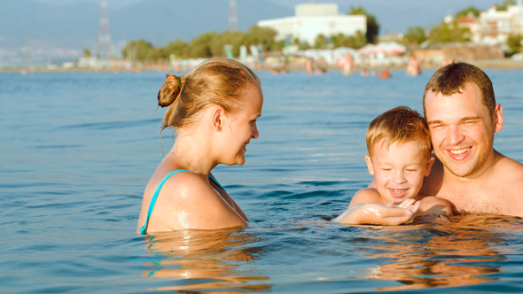 Happy Parents And Son Bathing In Sea On Resort