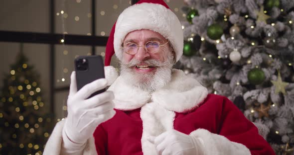 Kind Elderly Santa Claus Talking By Video Call Greeting His Interlocutor and Showing Thumb Up to