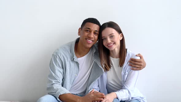 Excited Happy Multiracial Young Couple in Love Sitting on Sofa in Living Room of Their New Home