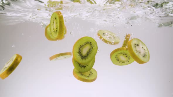 Slices of Kiwi Fall Down in Clear Water on White Background