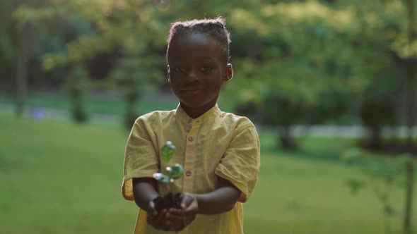 Portrait of Black Child Posing Outdoors with Sprout in Hands