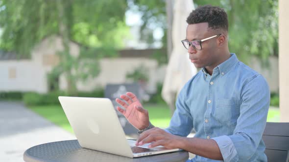 African Man with Coffee Working on Laptop in Outdoor Cafe