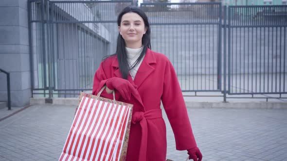 Middle Shot Front View of Elegant Young Lady in Red Coat Walking in City with Shopping Bags