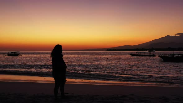 Silhouette of a woman with outstretched hands on the tropical sandy beach during the purple sunset