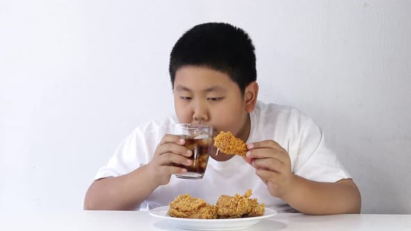 Asian fat boy eating fried chicken and drinking sweet water Wear a white shirt