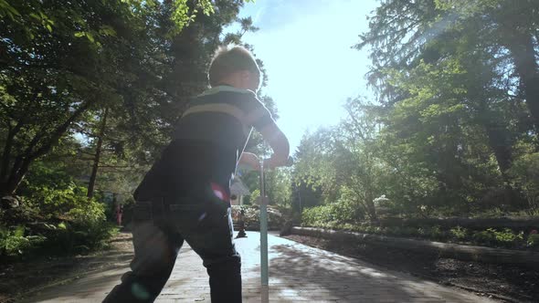 Little Boy Rides Scooter in the Park on Sunny Day