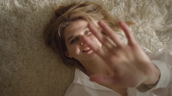 Close-up Portrait of Smiling Caucasian Blond Woman Lying on Soft Bed in Sunrays. Happy Young Girl