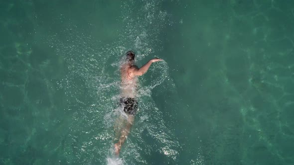 Aerial view of a man swimming in transparent water in Syros island, Greece.