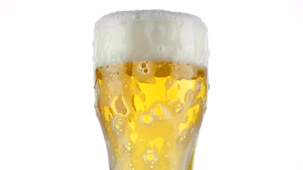 Pour light beer into a glass, foam flows out of the glass, white background. 4K UHD video