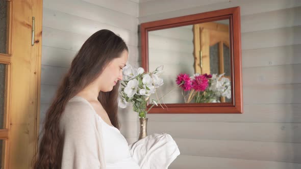 Cute Happy Pregnant Woman Pulls Out Baby Clothes From Dresser Touching Her Tummy at Home