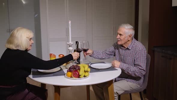 Cheerful Senior Couple Enjoying Romantic Supper Drinking Red Wine. Elderly Old People in Kitchen