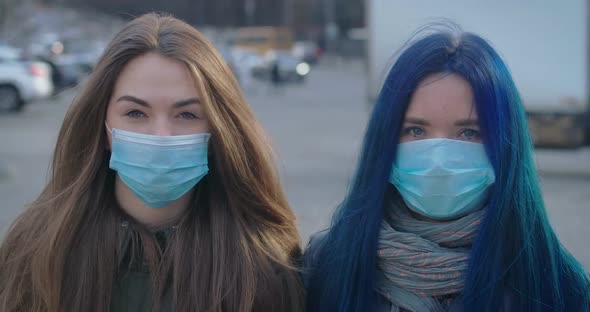 Close-up Faces of Two Young Women in Protective Masks Looking at Camera at the Background of Busy