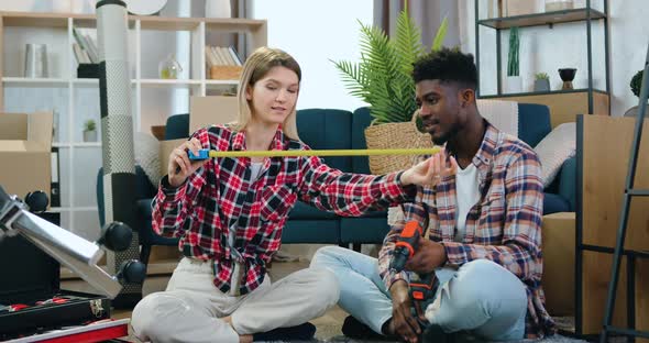 Couple Sitting on the Floor in Their New Flat and Using Tape Measure Measuring the Dimentions