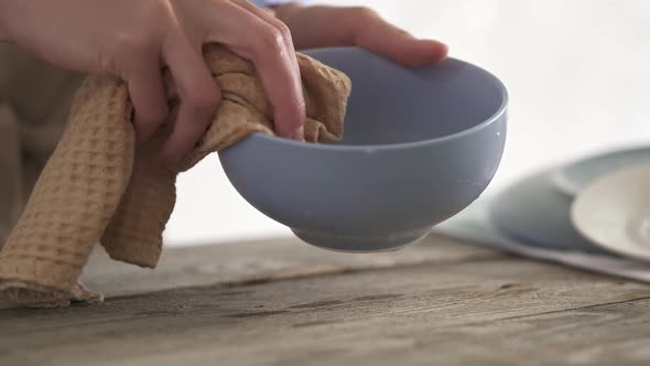 A young housewife in an apron wipes the dishes with a towel.