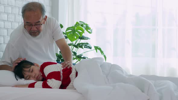 Elderly grandfather touching head of grandchild on bed to sleep with love at home