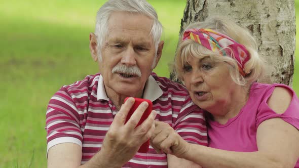 Family Picnic. Senior Old Grandparents Couple in Park Using Smartphone Online Browsing, Shopping