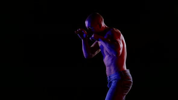 a Muscular Bald Man with a Bare Torso and Jeans is Boxing on a Black Background