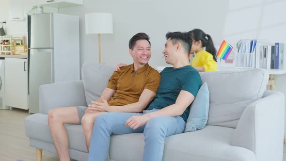 Asian attractive LGBTQ gay family sit on sofa, playing with young girl kid in living room at home.