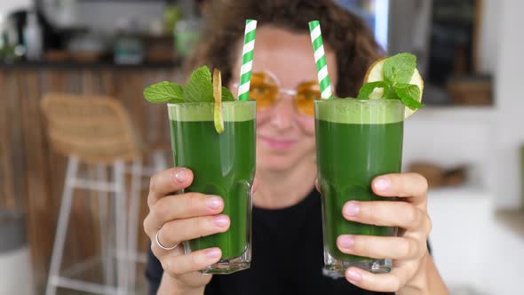 Caucasian Girl Showing to the Camera Two Green Smoothies with Paper Straws