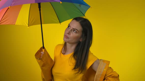 Attractive Woman in a Bright Raincoat with a Rainbow Umbrella in Yellow Studio