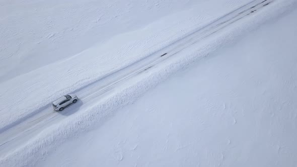 Aerial View on Car Driving Through Winter Forest Road Between the Snowcovered Fields