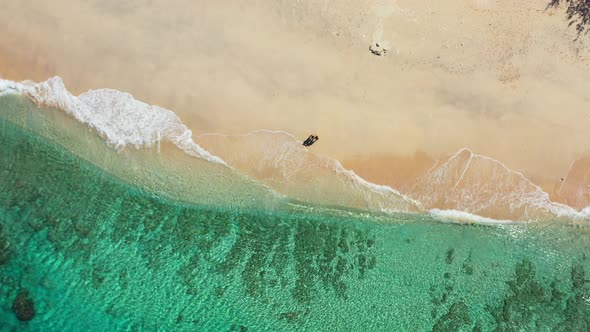 Antigua aerial. Young couple dancing on the white sand beach while foamy waves washing the shore. Cr