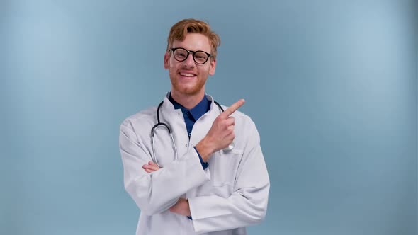 Portrait of Cheerful Young Medical Doctor Smiling at Camera and Points to the Side Isolated on Blue