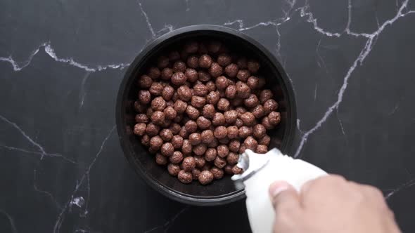 Top View of Pouring Milk on Chocolate Corn Flakes in a Bowl