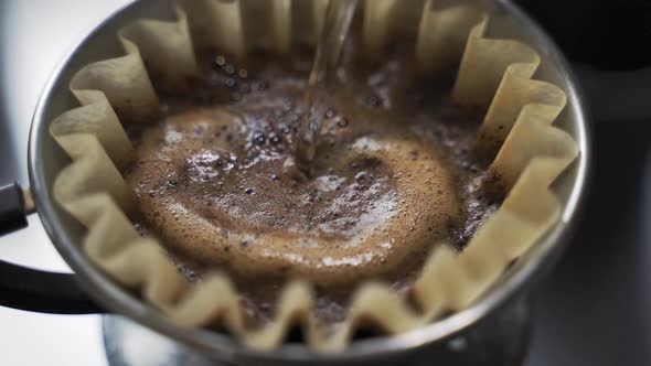 Slow motion pouring hot water over freshly ground coffee beans on filter paper