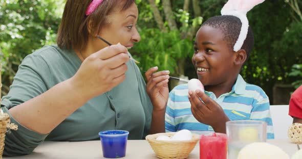 Animation of happy diverse grandmother and grandson painting easter eggs in garden