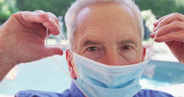 Portrait of senior caucasian man with grey hair putting face mask on looking at camera in slow motio