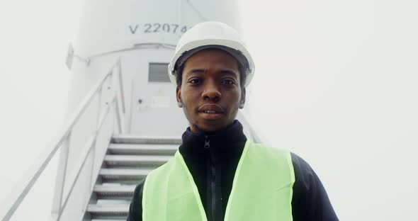 A Man Smiles Looking at the Camera Standing Near an Industrial Wind Turbine