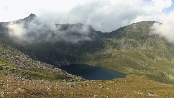 Timelapse of wind blows the fog over a beautiful deep blue mountain lake.